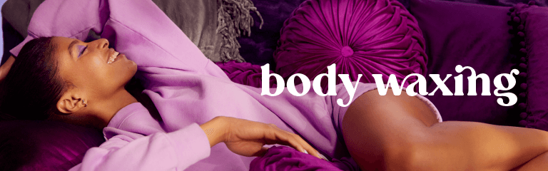 Body waxing in white text superimposed over a woman of color lounging on a deep purple couch wearing light purple sweats and smiling