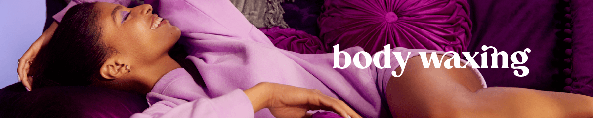 Body waxing in white text superimposed over a woman of color lounging on a deep purple couch wearing light purple sweats and smiling